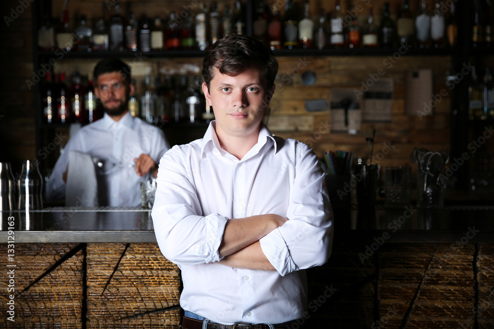 Man with crossed arms standing near wooden bar counter Man with crossed arms standing near wooden bar counter