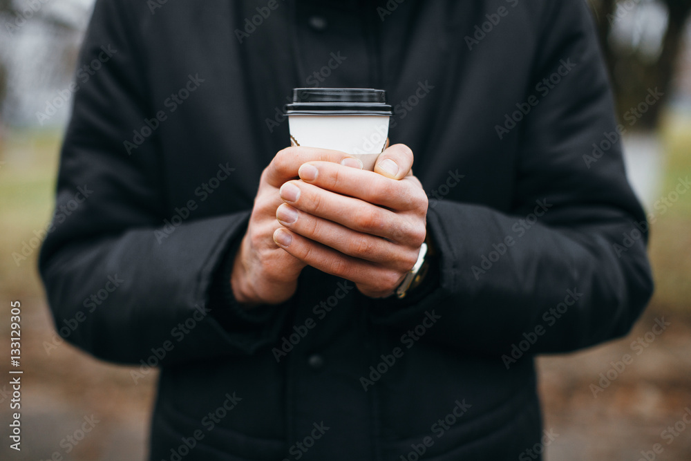 The guy holds a coffee Cup in hand on the street. The guy holds a coffee Cup in hand on the street.