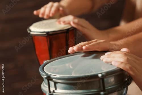 Hands of man playing African drum on dark background