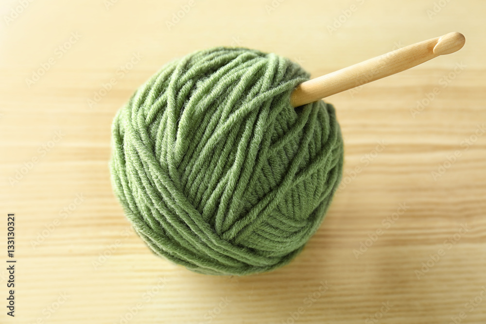 Green ball of knitting yarn and hook on wooden table