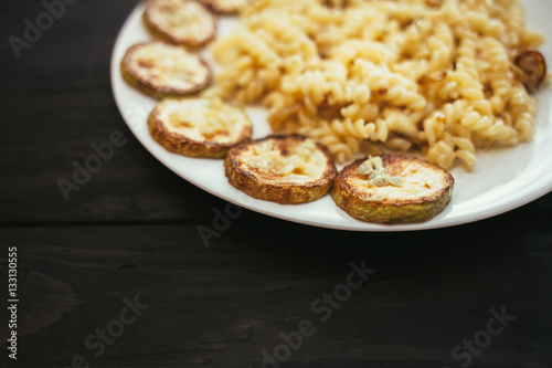 Pasta with fried zucchini on the plate on wooden background.