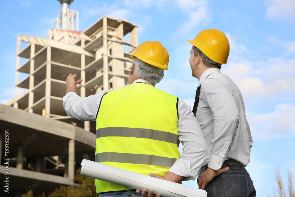 Engineer and worker discussing construction of unfinished building Engineer and worker discussing construction of unfinished building