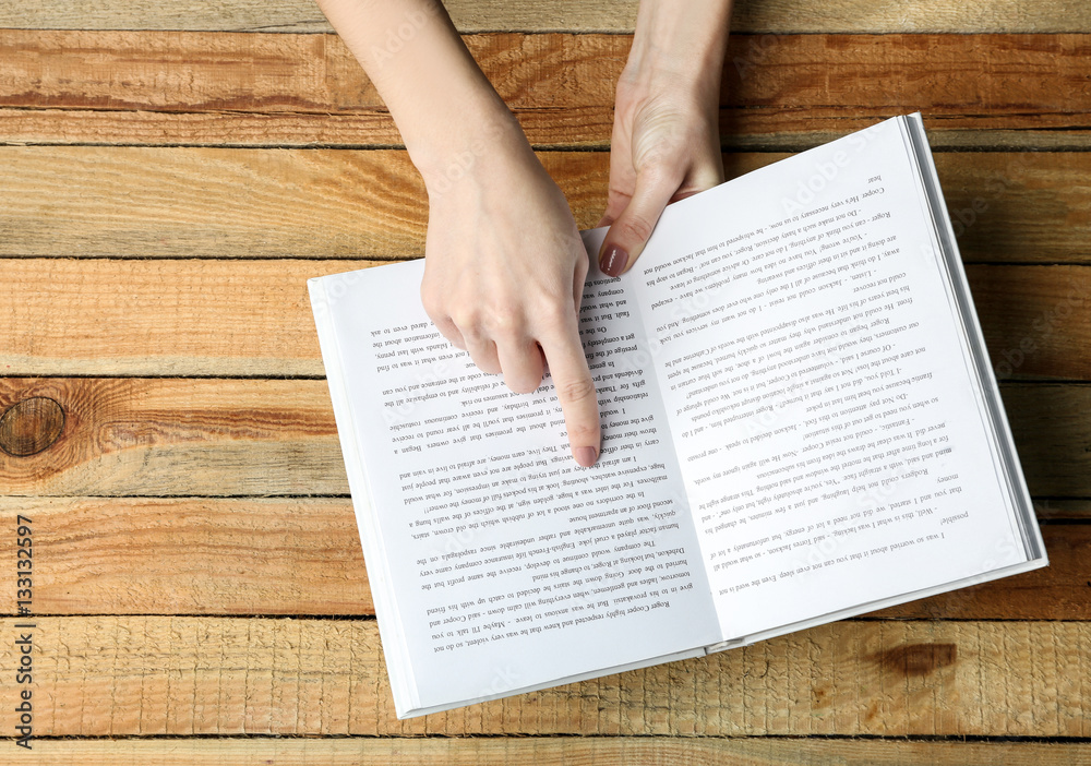 Naklejka premium Female hands holding opened book on wooden background