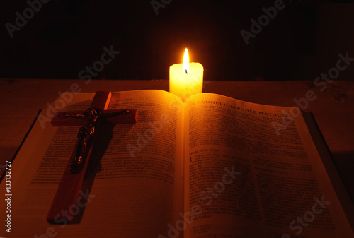 Burning candle, bible and crucifix on desk