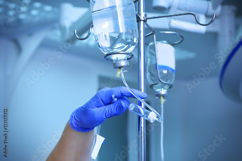 Doctor's hand and infusion drip in hospital on blurred background photo