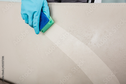 Close-up Of Person's Hand Cleaning Cushion Sofa Furniture