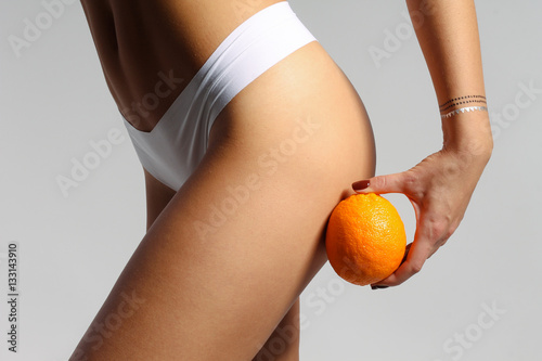 Mid section of sporty woman holding orange near her leg, anti-cellulite concept 