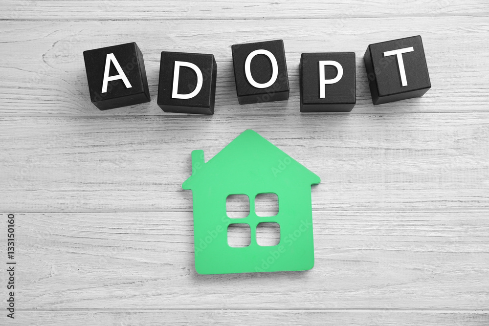 Black cubes with word ADOPT and figure in shape of house on light wooden background Black cubes with word ADOPT and figure in shape of house on light wooden background