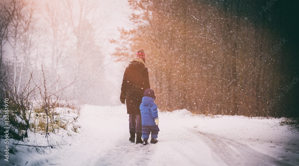 Mother and baby walking by sandy forest road in wintertime Mother and baby walking by sandy forest road in wintertime