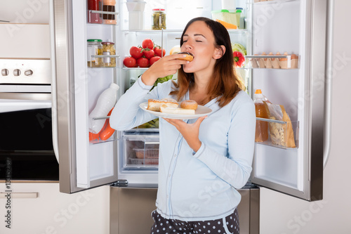 Photographie Woman Eating Sweet Food Near Refrigerator