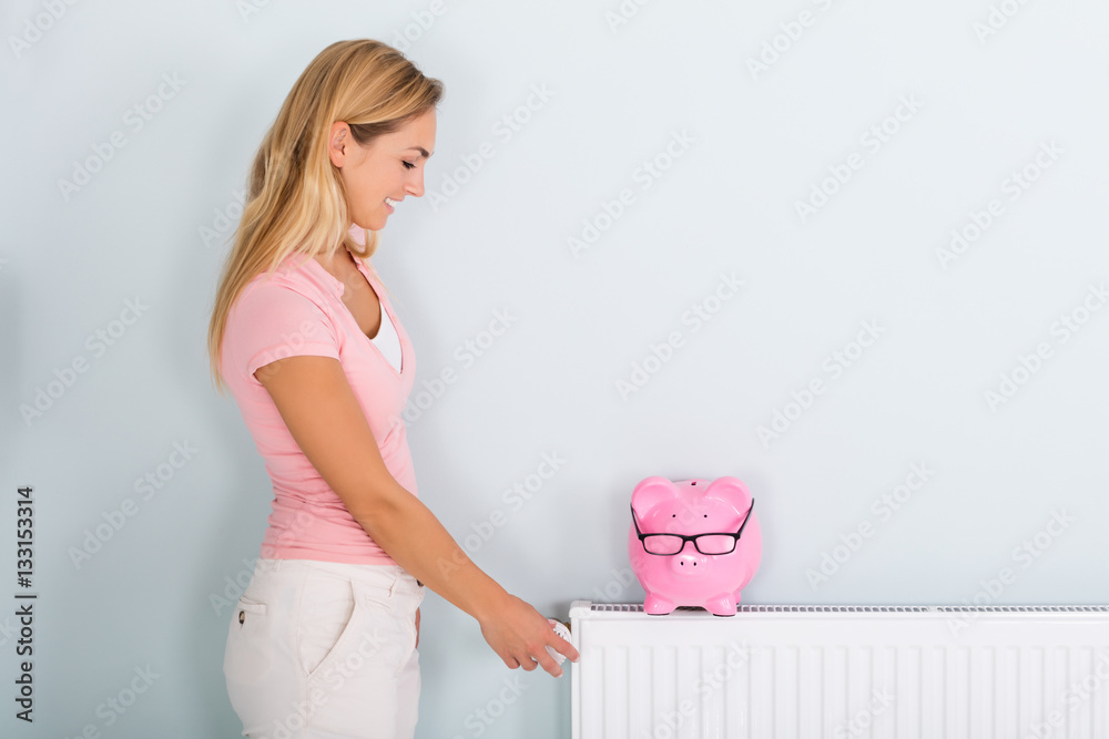 Φωτογραφία Woman Adjusting Thermostat With Piggy Bank On Radiator