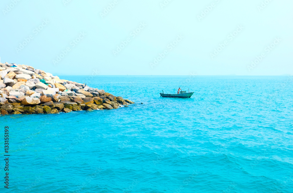 Man in a longtale boat in the turquoise sea. Secluded rocky island. Thailand