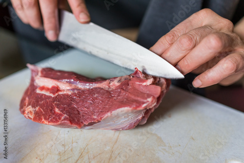 Hands with large knife cutting whole beef roast