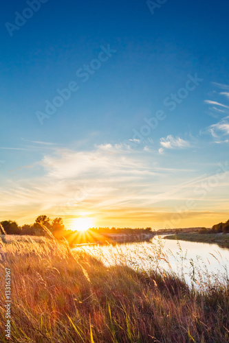 Sunset on the river bank covered with grass meadow