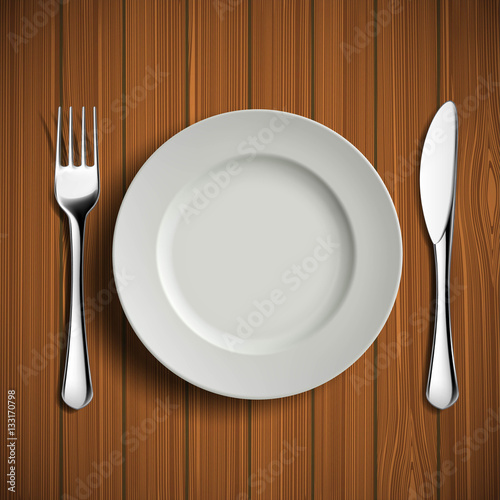 White ceramic plate, fork and knife on a wooden table. Table lay