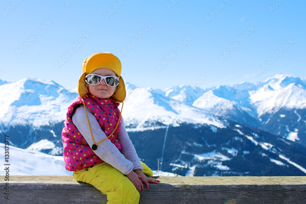 Happy child enjoying winter holidays in Alpine resort in Austria. Little girl playing in the snow. Kids having fun outdoors. Beautiful Alps mountains in the background.