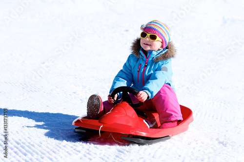 Happy child enjoying winter vacation in Alpine resort in Austria. Little girl playing in the snow. Active sportive toddler riding sledge.