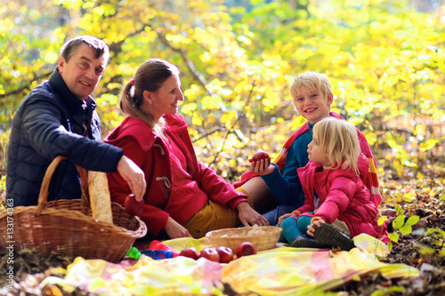 Family with kids having picnic in the forest. Mother, father and two children enjoying warm sunny autumn day in the nature. Fall fun outdoors.