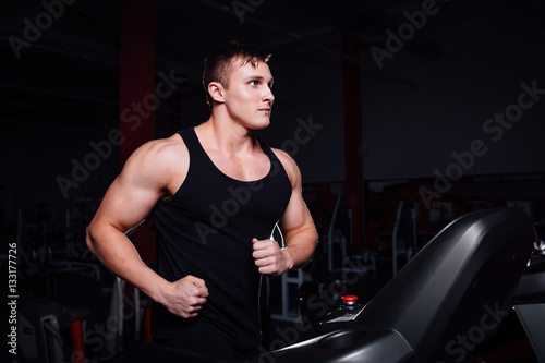 Young strong big man fitness model in the gym running on the treadmill with water bottle.