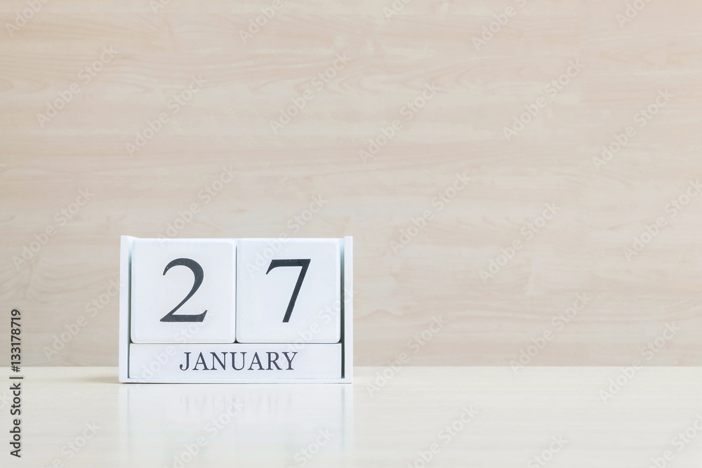 Closeup surface white wooden calendar with black 27 january word on blurred brown wood desk and wood wall textured background with copy space , selective focus at the calendar Closeup surface white wooden calendar with black 27 january word on blurred brown wood desk and wood wall textured background with copy space , selective focus at the calendar