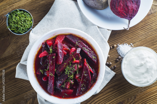Vegetable soup - red borsch  in a white bowl on a rustic wooden background, top view. Healthy beetroot soup, vegetarian food. Delicious beet soup with sour cream, flat lay. photo