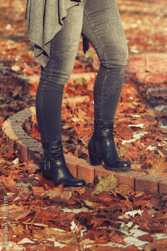 Woman's legs in black jeans and black high heel boots standing in the park in fallen leaves