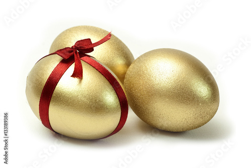 Three Easter Gold eggs with red ribbon cross and bow on white background isolated.