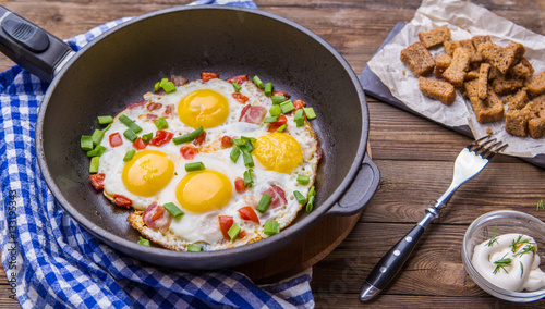 Fried eggs in pan with tomatoes and green fresh onion.