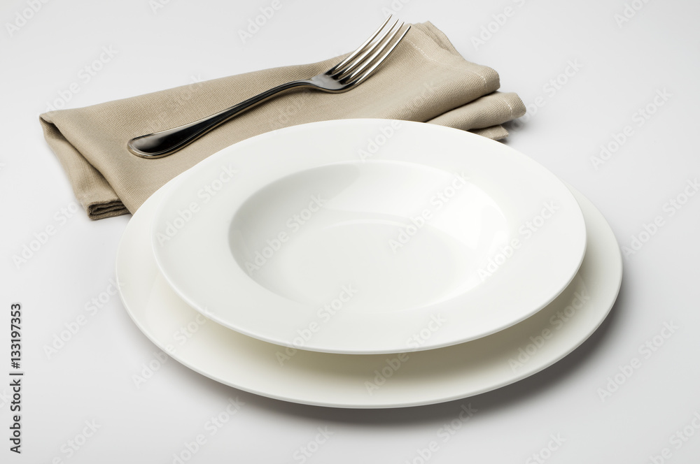 Empty round white plate and bowl with napkin and fork