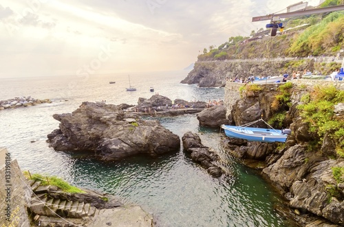 Manarola town,Riomaggiore,La Spezia province,Liguria,northern Italy.View of the beach at sunset and a crane lifting a boat from rocks. Part of Cinque Terre National Park and UNESCO World Heritage Site