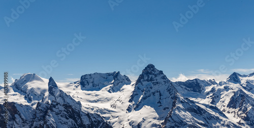Snowy mountain peaks against the blue sky. © VASILEVS