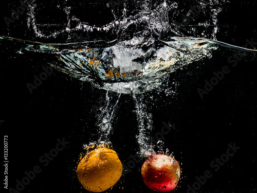 Apple and orange falling in water on black background.