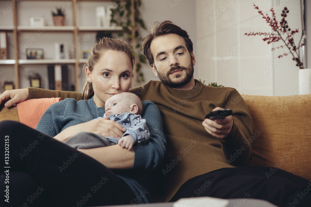 Father and mother sitting with baby on couch watching Tv Father and mother sitting with baby on couch watching Tv