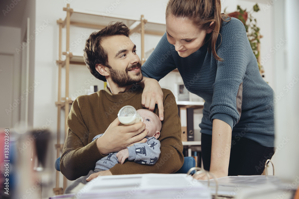 Mother looking at father feeding baby in home office Mother looking at father feeding baby in home office