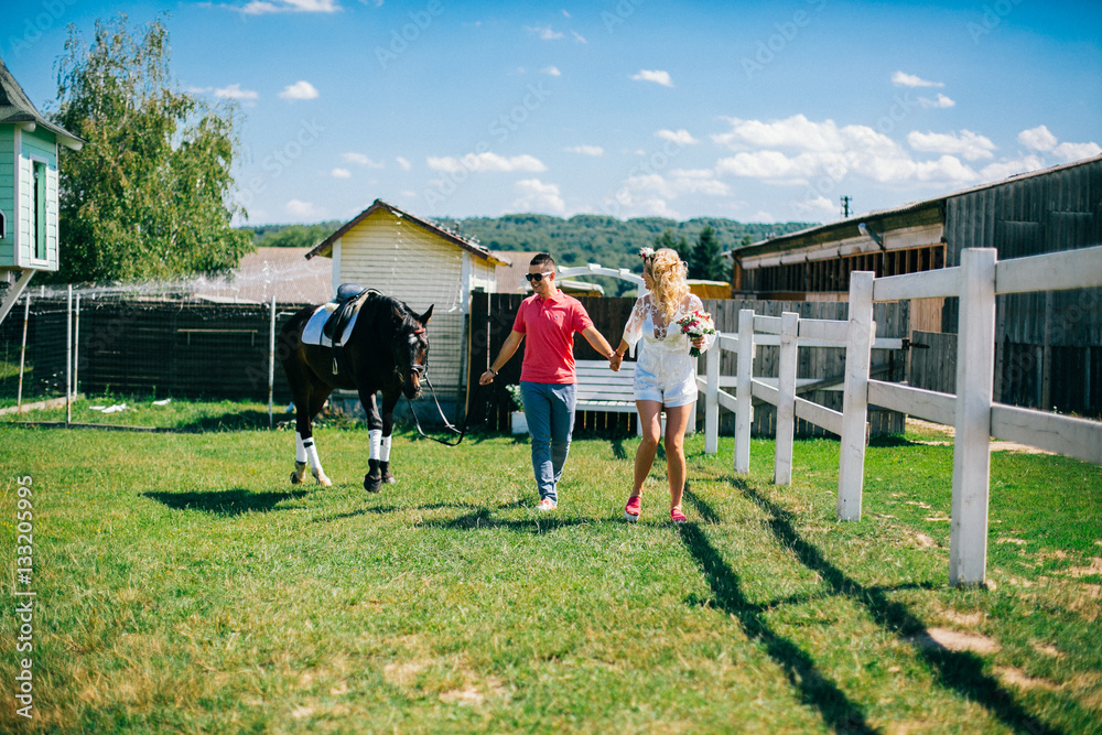 Obraz premium Young couple stay and walking near black horse at green farm