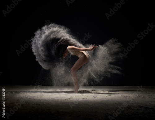 Fotografie Dancer moving in cloud of white dust at studio