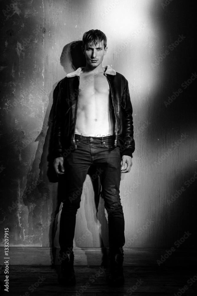 handsome young man in black jacket posing in studio. Sexy young man with muscular body and bare torso