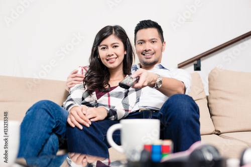 Asian couple on sofa in living room changing tv channel