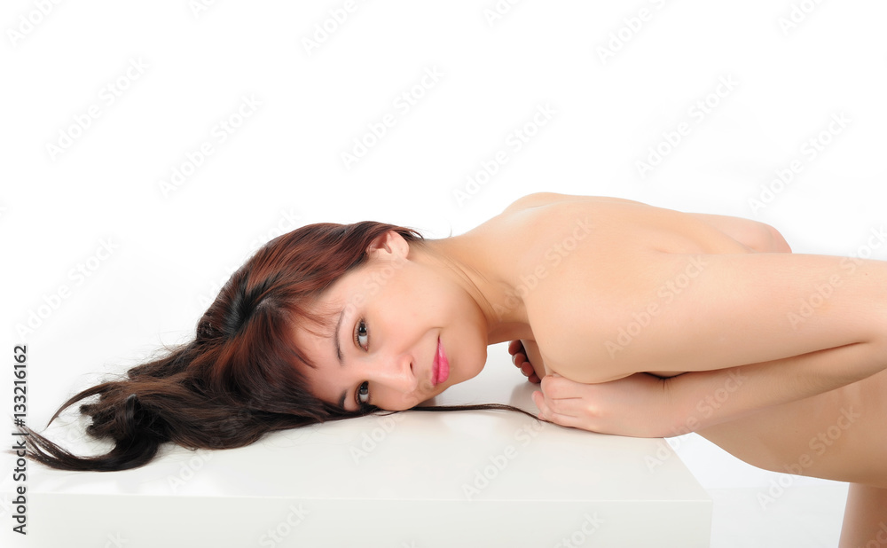 Young long-haired naked brunette leans on a white table on a white background Young long-haired naked brunette leans on a white table on a white background
