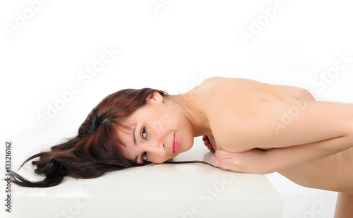 Young long-haired naked brunette leans on a white table on a white background