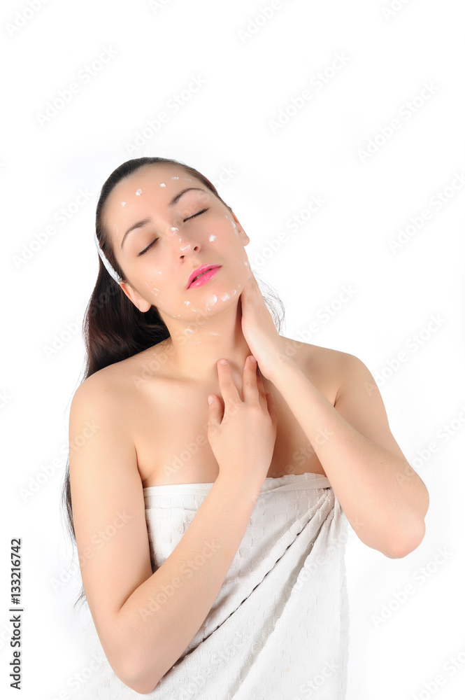 Young long-haired brunettein towel applies the cream to face on a white background Young long-haired brunettein towel applies the cream to face on a white background