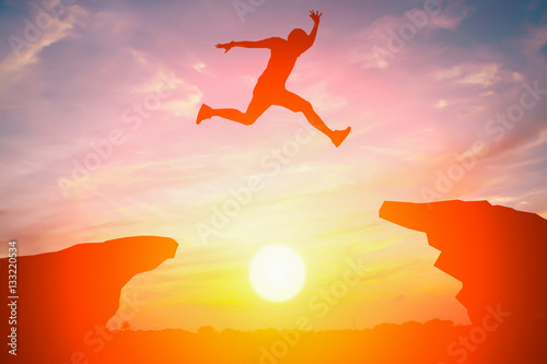 Silhouette of man jump over the cliff obstacle in sunset