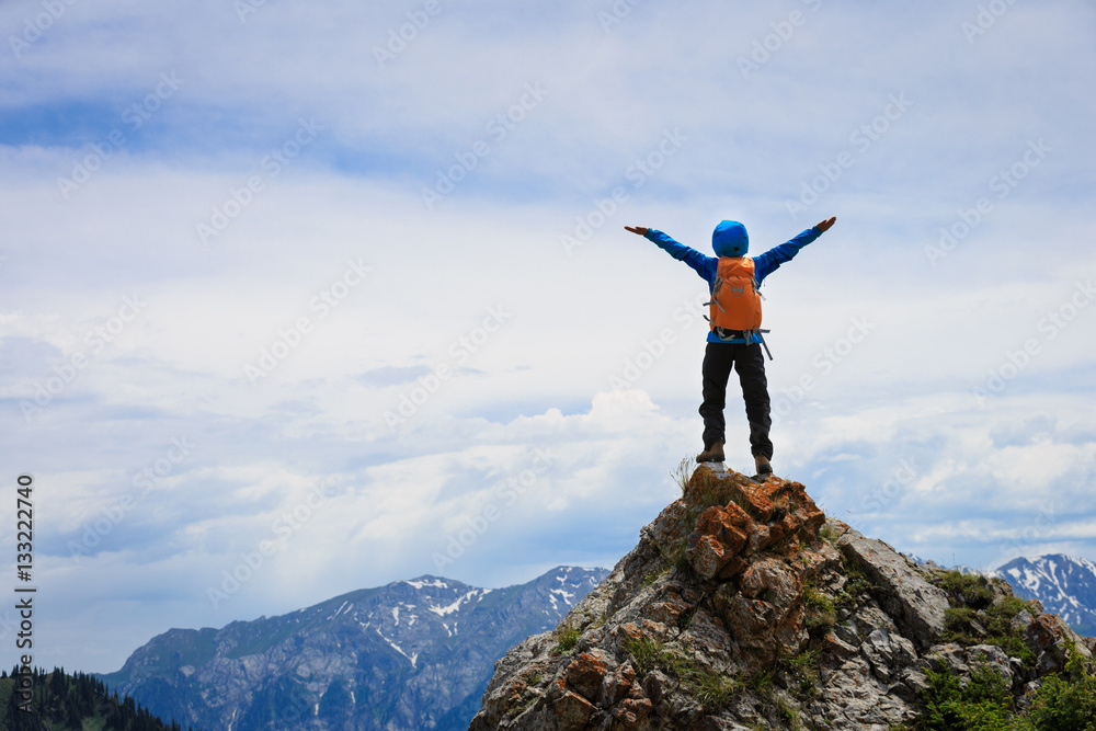 Obraz premium successful young woman backpacker open arms on mountain peak