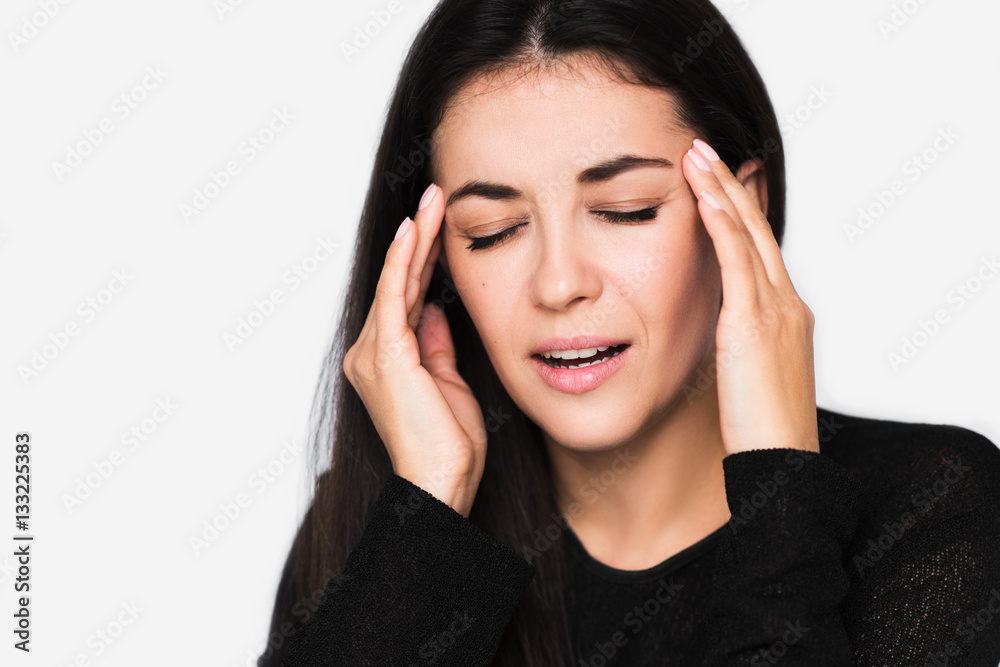 Close up portrait of brunette pretty woman with headache touching her temples. Young beautiful woman stressed wearing black sweater on light grey background. Unhappy mood. Healthcare and medicine. Close up portrait of brunette pretty woman with headache touching her temples. Young beautiful woman stressed wearing black sweater on light grey background. Unhappy mood. Healthcare and medicine.