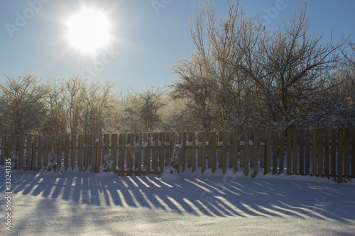 Winter snowy vintage old backyard wooden fence, beautiful shadows on sunny snow