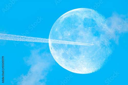 Airplane with trail of fuel on blue sky and big moon"Elements of this image furnished by NASA
