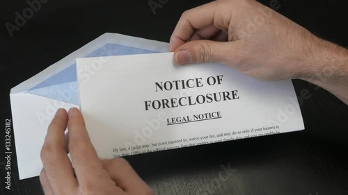 Hands opening an envelope containing a Notice of foreclosure document. Top view from above. photo