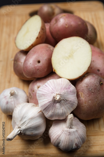 Pile of potatoes with garlic on wood board with black background