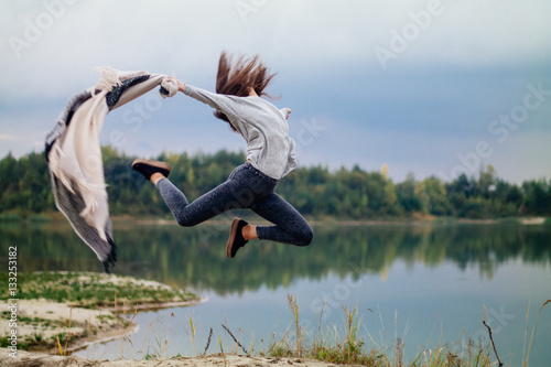 Extreme fit girl jump near lake with rug in hand