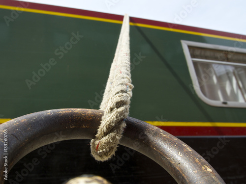 Canal boat mooring, rope attached to a rusted ring with boat in the background with window, looking up close